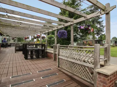 a wooden pergola with a table and benches on a deck at Stables Cottage in Leominster
