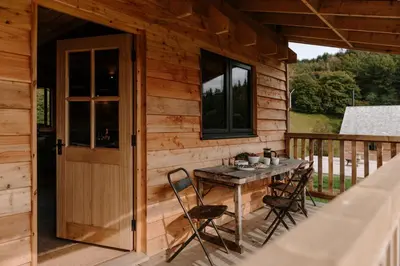 a wooden cabin with a table and chairs on a deck at Woolly Wood Cabins - Bryn in Llandrindod Wells