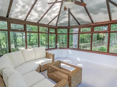 a conservatory with a white couch and chairs and windows at The Coach House at Plas Dolguog in Machynlleth