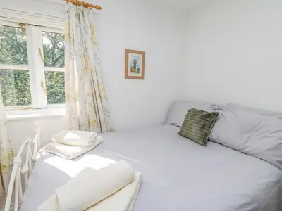 a white bedroom with a bed and a window at The Coach House at Plas Dolguog in Machynlleth