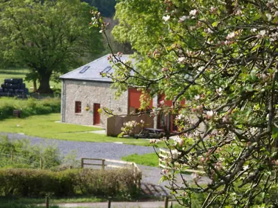 a stone building with a red door in a yard at Peregrine Stable Cottage in Llandovery