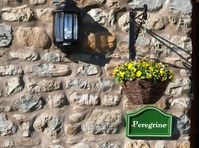 a sign on a stone wall with a basket of flowers at Peregrine Stable Cottage in Llandovery