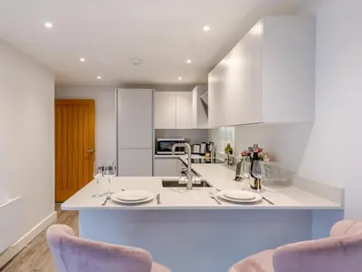 a white kitchen with two chairs and a counter at Bouvardia Modern town centre apartment - Pass the Keys in Shrewsbury
