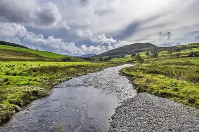 a river in the middle of a grassy field at Finest Retreats - Mountain View in Trawsfynydd