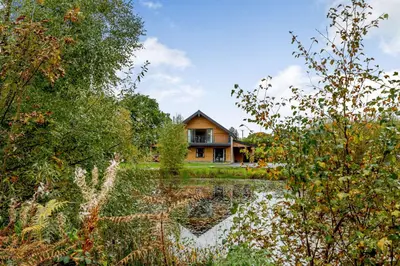 a house with a pond in front of it at Rhosllyn Retreats - Lakeside Lodge in Rhayader