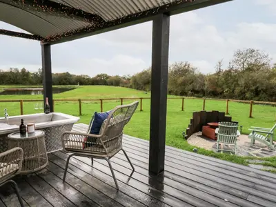 a deck with chairs and a tub and a view of a field at Dragonfly Shepherd's Hut in Aberaeron