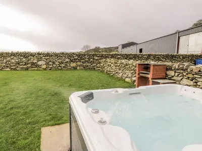 a hot tub in a yard next to a stone wall at Hay Store in Corwen