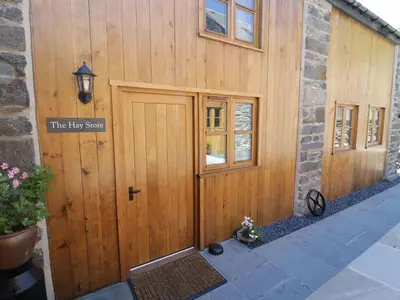 a wooden building with a door with a sign on it at Hay Store in Corwen