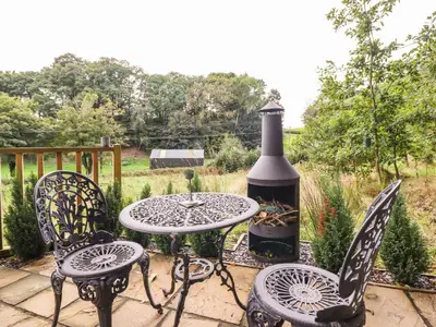 a patio with a table and chairs and a bottle of wine at Chateau Petit in Caersws