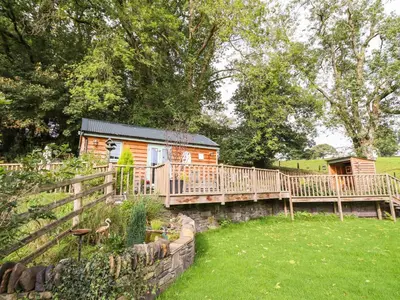 a cabin with a wooden deck in a yard at Chateau Petit in Caersws