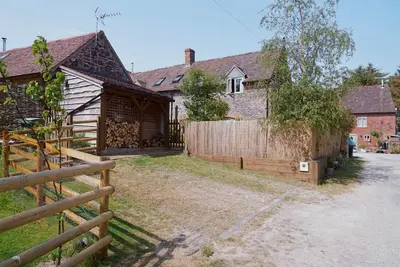 a house with a wooden fence next to a yard at Nest Holiday Hideaway Dove Cottage-Beautiful Location in the Long Mynd Area of Outstanding Natural Beauty-WHIRLPOOL JACUZZI BATHS!! in Picklescott