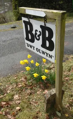 a sign on the side of a road with yellow flowers at Dwy Olwyn in Dolgellau