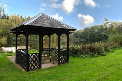 a wooden gazebo with a bench in the grass at Lake House in Brecon