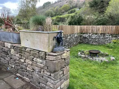 a stone retaining wall with a fountain in a yard at Transformed Railway Wagon- Sleeps2-Garden-Firepit in Crickhowell
