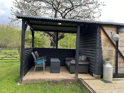 a black shed with a couch and a chair on a deck at Transformed Railway Wagon- Sleeps2-Garden-Firepit in Crickhowell