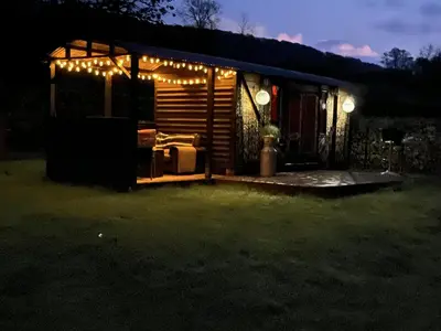 a cabin lit up at night with lights on it at Transformed Railway Wagon- Sleeps2-Garden-Firepit in Crickhowell