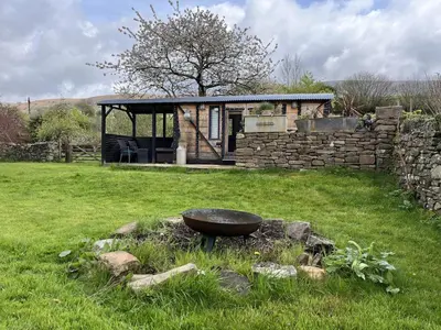 a garden with a stone building and a bowl in the grass at Transformed Railway Wagon- Sleeps2-Garden-Firepit in Crickhowell