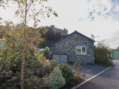a small stone house with a castle in the background at Tan Isa in Harlech