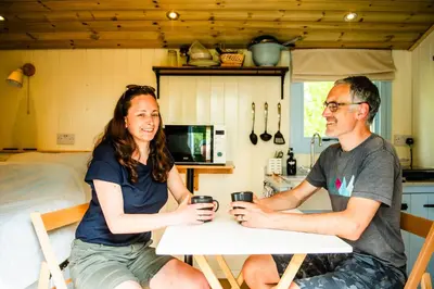 a man and woman sitting at a table with drinks at Cosy Shepherd's Hut with Hot Tub in Church Stretton