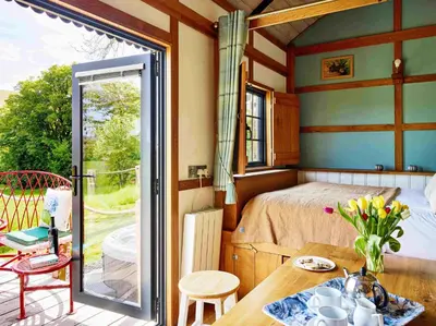 a room with a bed and a table and a balcony at The Orient Express Shepherd's Hut with Hot Tub in Brecon