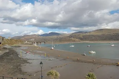 a beach with boats in the water and mountains at Beach Vista Apartment Three in Barmouth in Barmouth