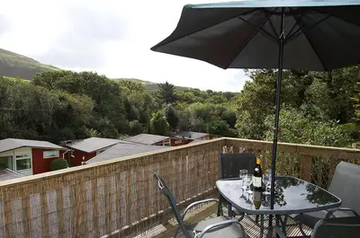 a table and chairs with an umbrella on a balcony at Bryniau Gwyrdd Chalet 11 Happy Valley in Tywyn