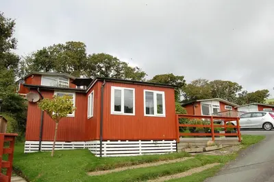 a red and white house with a car parked next to it at Bryniau Gwyrdd Chalet 11 Happy Valley in Tywyn