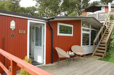 a red tiny house with two chairs and a wooden deck at Bryniau Gwyrdd Chalet 11 Happy Valley in Tywyn