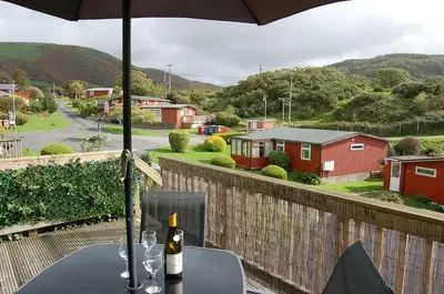a table with wine glasses and an umbrella on a balcony at Bryniau Gwyrdd Chalet 11 Happy Valley in Tywyn