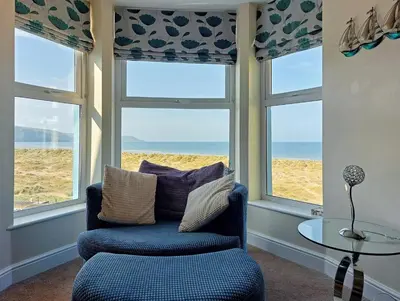 a living room with a chair and windows with a view of the beach at Hafan Y Traeth Beach Front Apartment in Barmouth in Barmouth