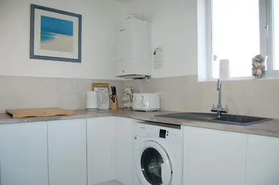 a white kitchen with a washing machine and a sink at Chwerthin Y Mor Beach House in Tywyn