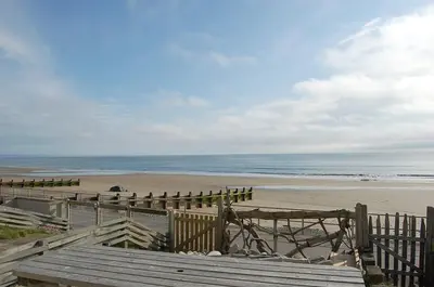 a view of a beach with a fence and the ocean at Chwerthin Y Mor Beach House in Tywyn