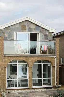 a brick house with large windows and a balcony at Ty Traeth Beach House in Tywyn