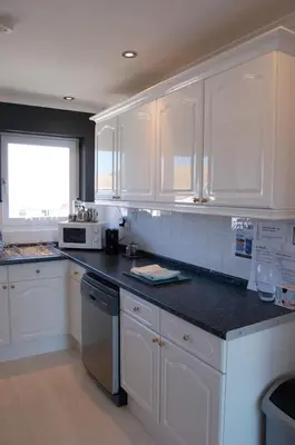 a kitchen with white cabinets and a black counter top at Tywyn Beach House in Tywyn
