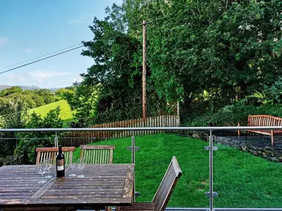a bottle of wine sitting on a wooden table with two chairs at Caer Dderwen Oak Field family home in Dolgellau in Dolgellau