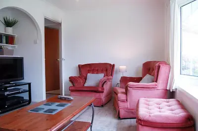 a living room with two pink chairs and a table at Hafan Y Talgarth bungalow at Plas Talgarth resort in Pennal