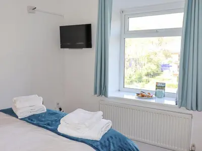 a bedroom with a bed with blue curtains and a window at No 9 On The Riverbank in Llangollen