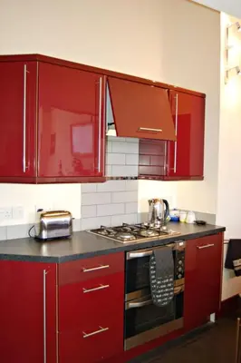 a kitchen with red cabinets and a stove top oven at Sand Dune Apartment in Barmouth in Barmouth