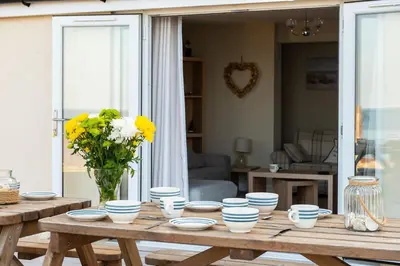 a wooden table with blue and white bowls and a vase of flowers at Sound of the Sea, beach front Bungalow with hot tub, in Tywyn in Tywyn