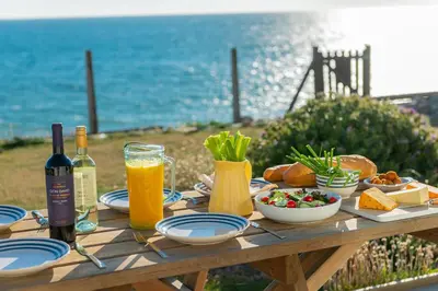 a picnic table with food and wine and the ocean at Sound of the Sea, beach front Bungalow with hot tub, in Tywyn in Tywyn