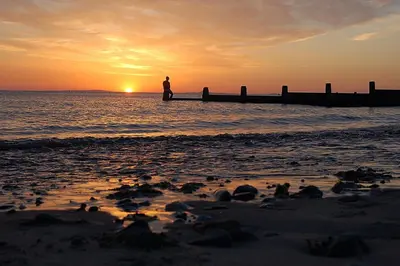 a person standing on the beach watching the sunset at Caravan 309 Bryn Y Mor Beach Side Park in Tywyn
