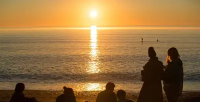 a group of people sitting on the beach watching the sunset at Penglais Lodge in Aberystwyth