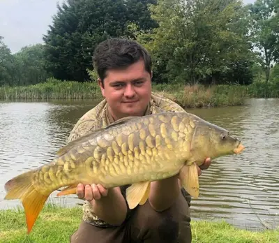 a man holding a fish in front of a pond at Mwsogl - Luxurious Family Fishing Lodge Near Aberaeron With Private Fishing in Cross Inn