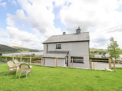 a white house with a table and chairs in the grass at Craig Yr Ronwy in Bala