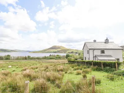 a white house in a field next to a body of water at Craig Yr Ronwy in Bala