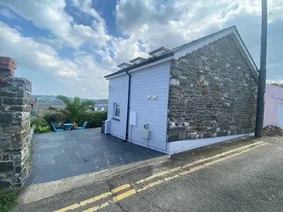 a small white building next to a stone wall at Y Stabl in New Quay