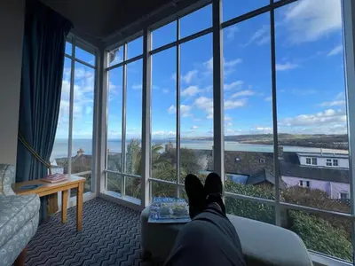 a person laying on a bed looking out of a window at Y Stabl in New Quay