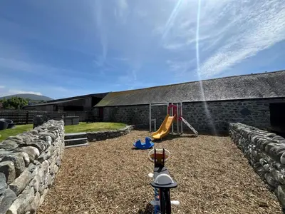 a backyard with a stone wall and a playground at 2 Bed in Dyffryn Ardudwy oc-89394 in Dyffryn