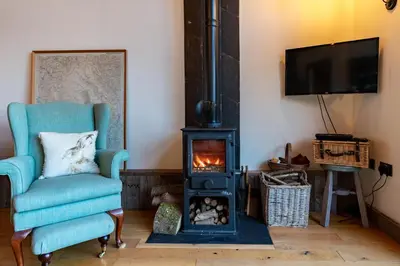 a living room with a blue chair and a wood stove at Outshot Barn in Hay-on-Wye