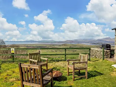 two wooden chairs sitting in the grass near a fence at 6 Bed in Harlech oc-91546 in Harlech